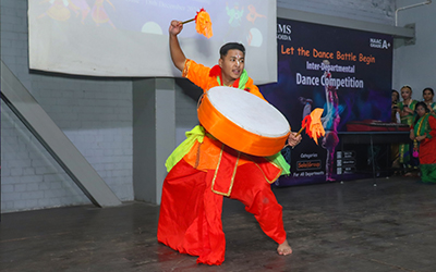 A student performing a dynamic dance with a drum at the Inter-Departmental Dance Competition at IMS Noida